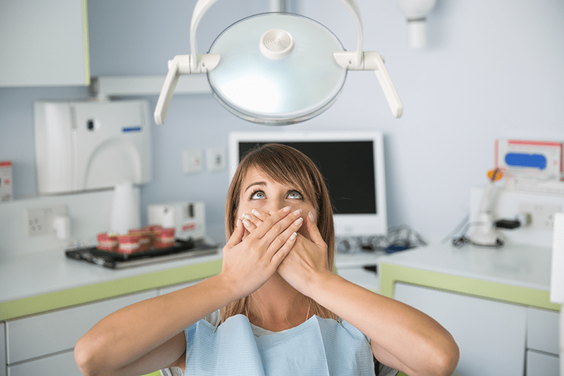 Woman sitting in dental chair with hands covering her mouth