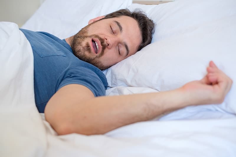 Man lies in bed with mouth open, commonly referred to as a mouth breather. A study has shown that it is common for those with upper airway obstruction on malocclusion patterns can cause issues with your teeth.