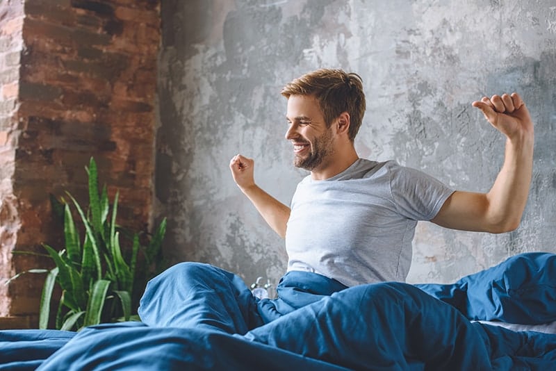 Handsome male professional from Burke stretches in the morning after a restful sleep. He's been able to fight his sleep apnea with a sleep appliance like MicrO2 offered by Dr. Pamela Marzban.